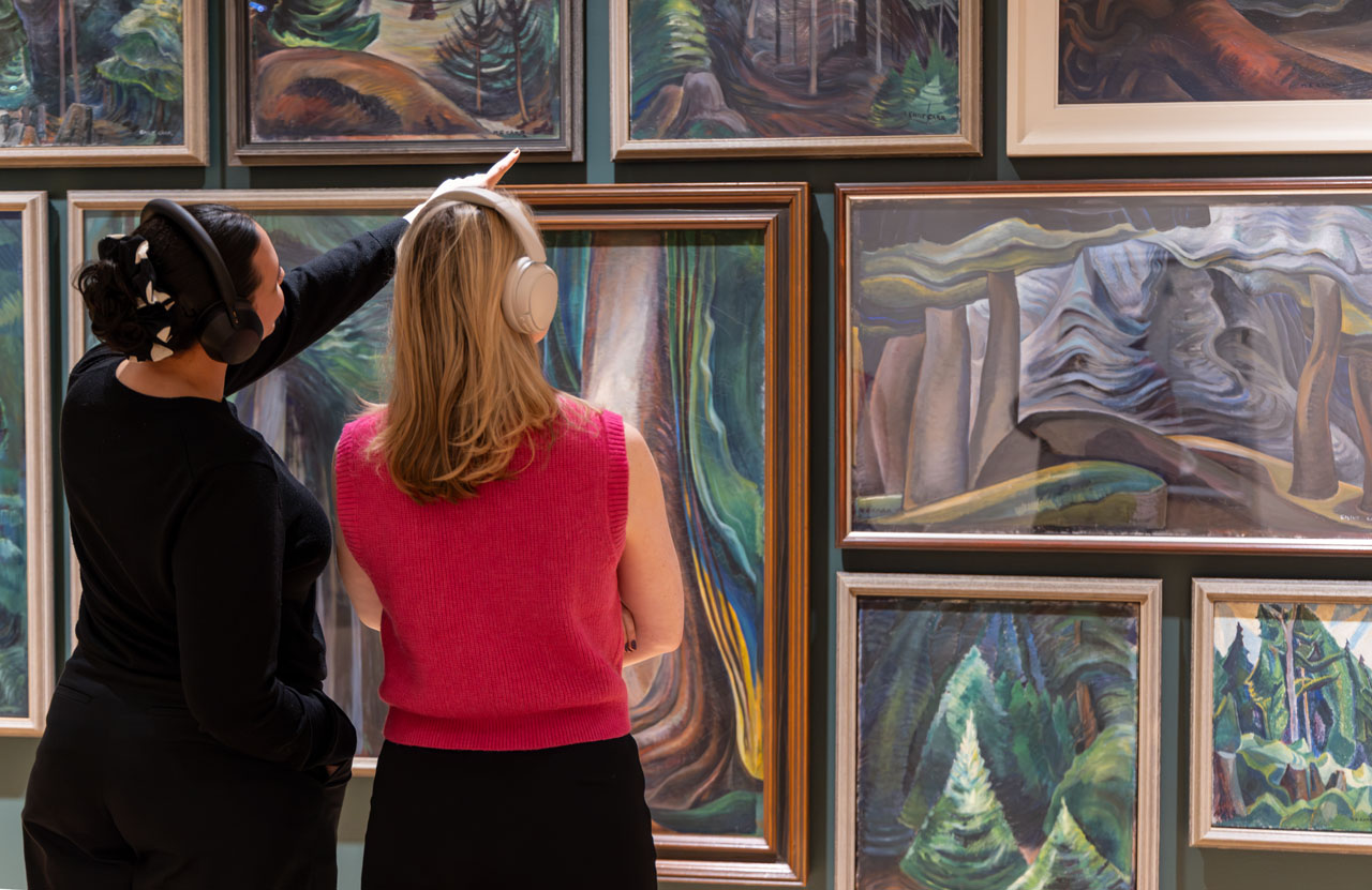 Two women looking at and discussing Emily Carr's forest paintings
